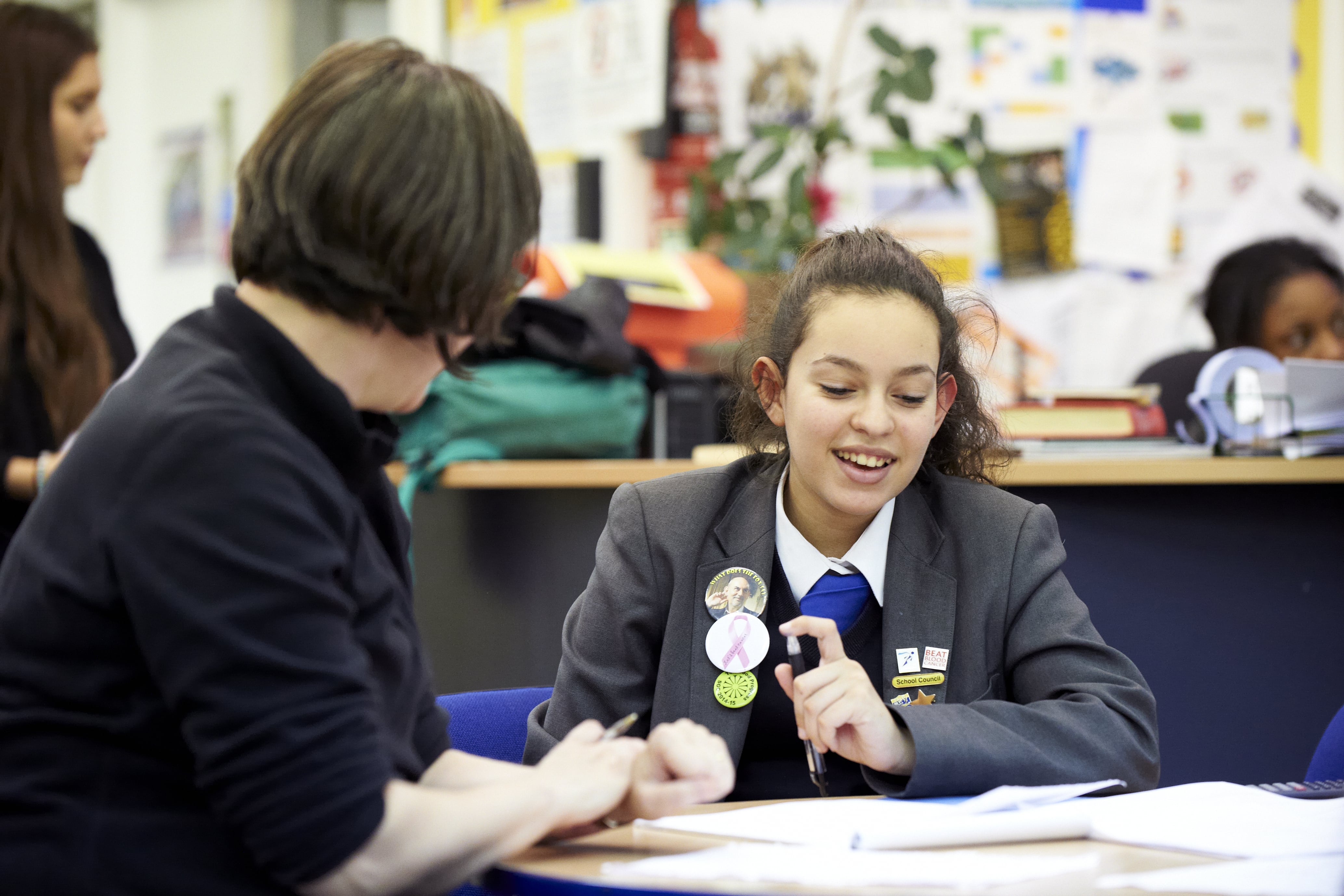 Teacher and school pupil speaking, sat at a classroom desk